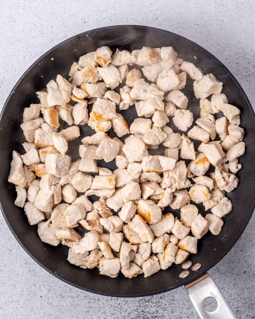 Chicken pieces cooking in a large pan.