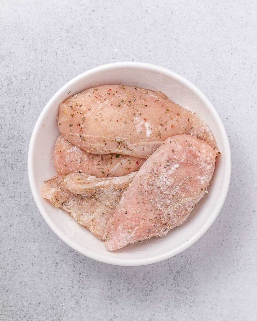 Seasoning chicken breasts in a white bowl.