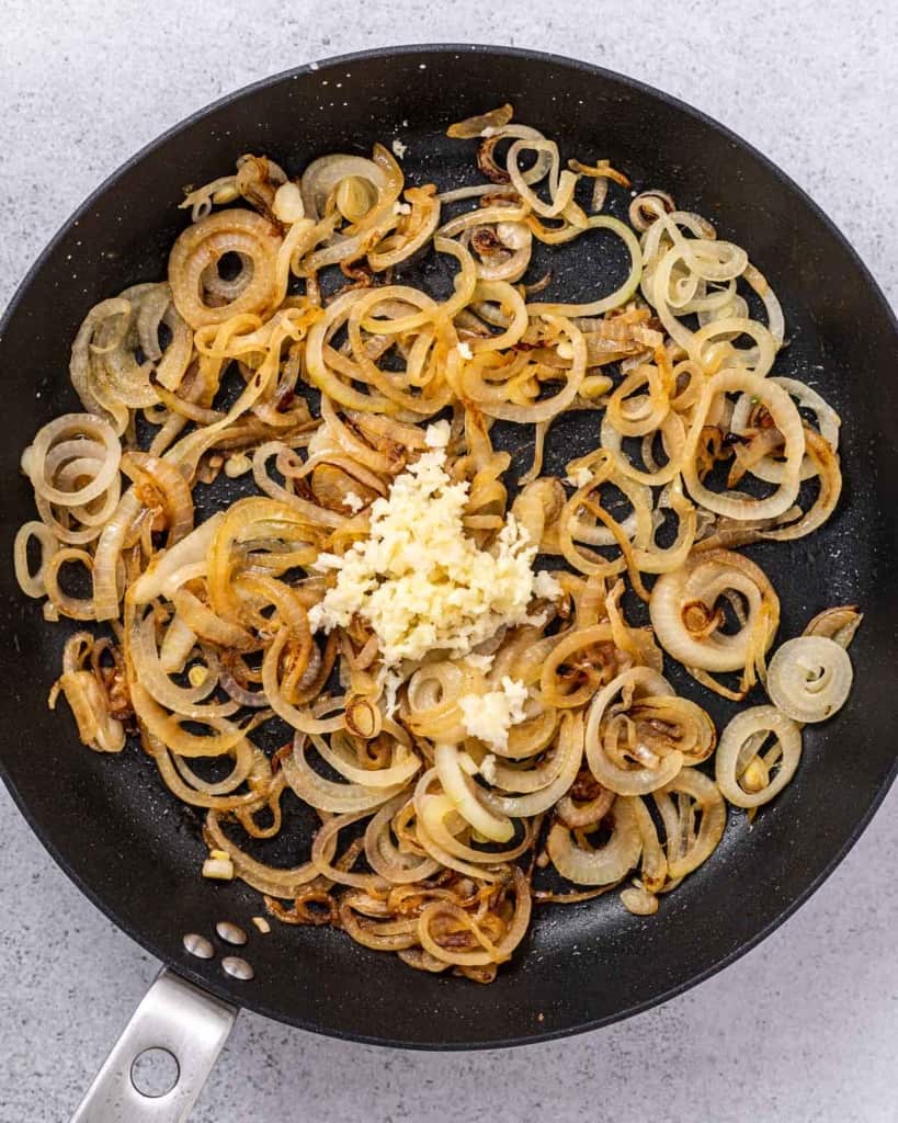 Adding pressed garlic to a pan with caramelized onions.