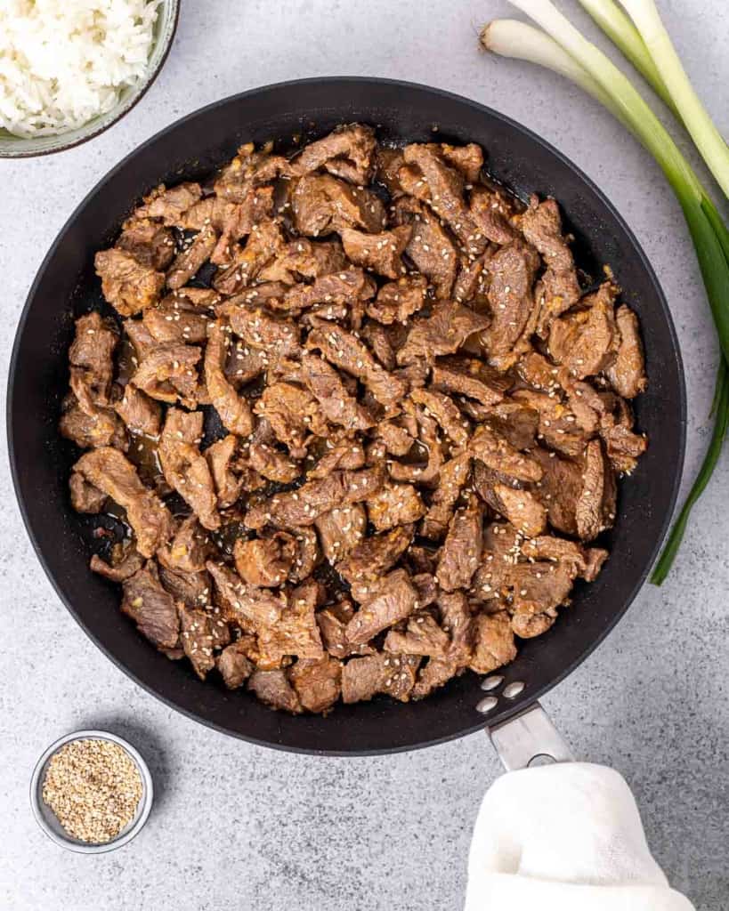Cooking thinly sliced beef in a large pan.