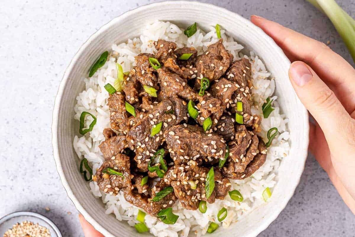 Woman's hands holding a bowl of bulgogi served over white rice.