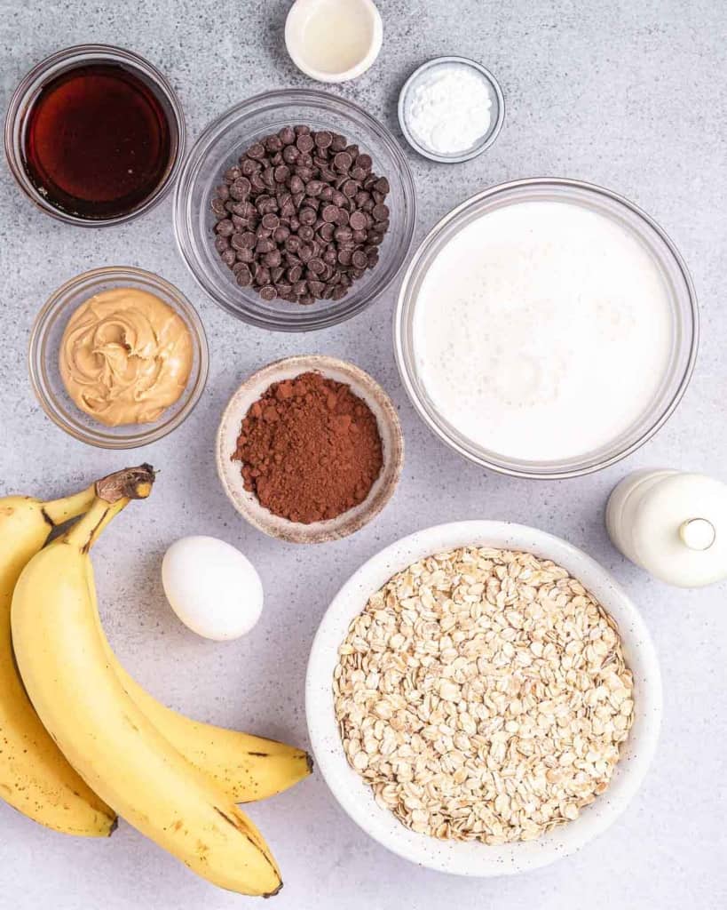 Ingredients for making peanut butter, chocolate, banana baked oatmeal divided into small bowls.