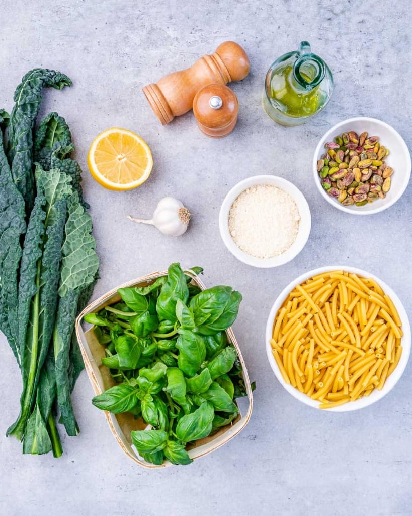 Uncooked pasta, fresh kale and basil and other ingredients divided into small portions.