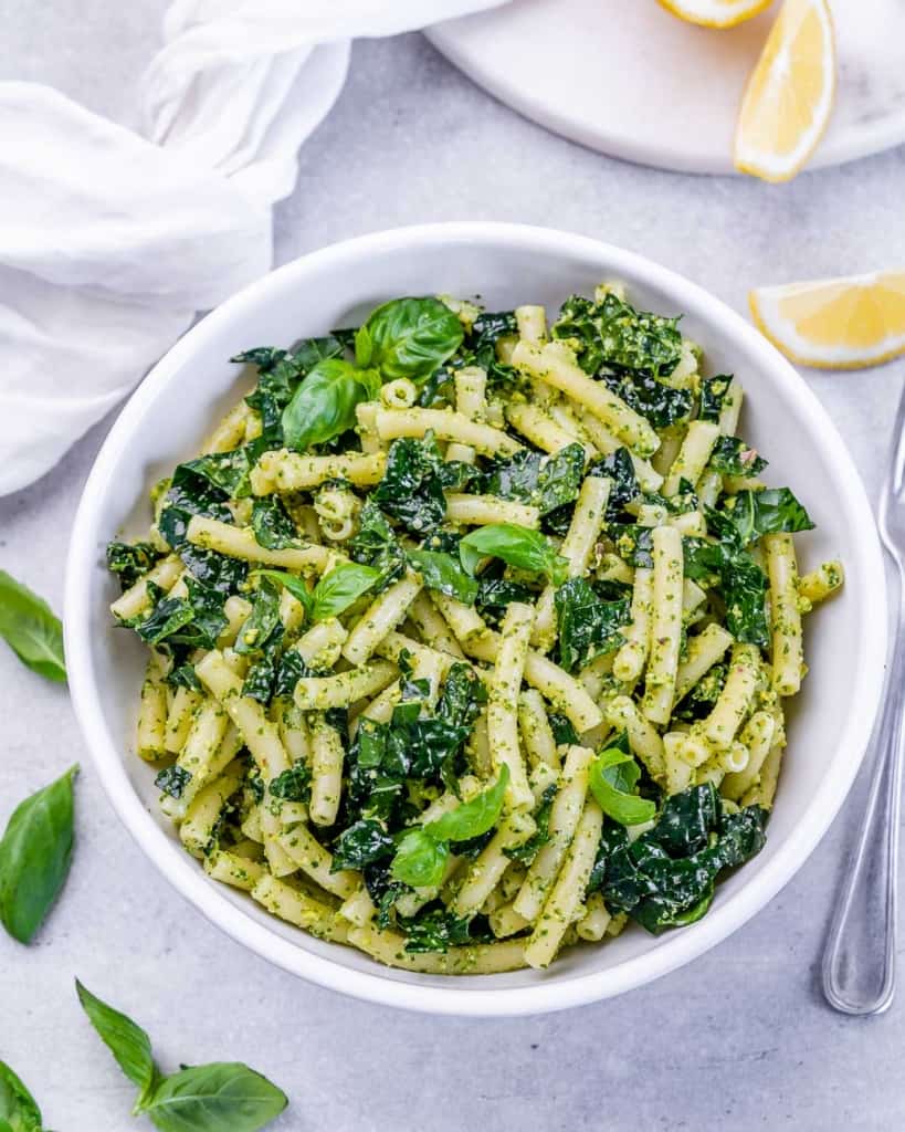 Pasta combined with pesto and kale in a large white bowl.