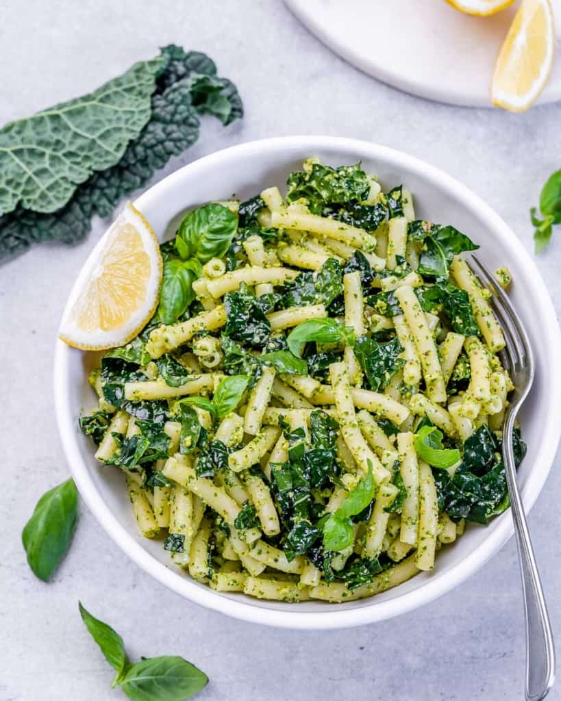 Pesto pasta in a white round bowl served with a lemon wedge.