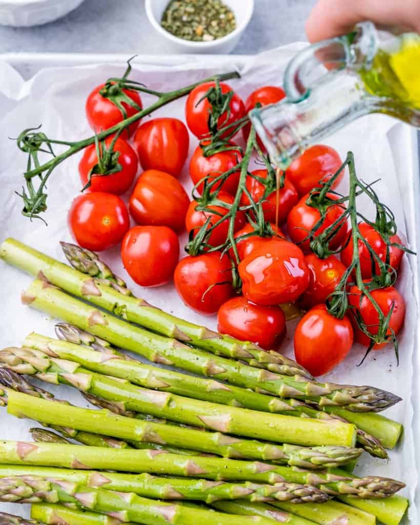 Placing cherry tomatoes on the vine and asparagus on a sheet pan.