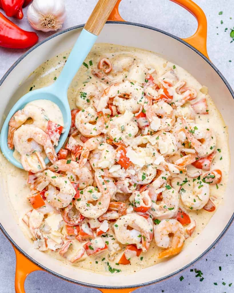 top view of creamy sauteed shrimp on an orange skillet with a baby blue spoon in pan
