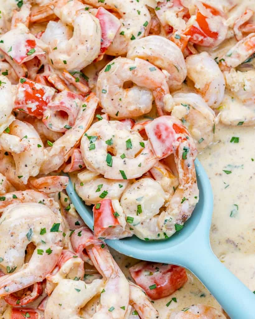 Spooning creamy shrimp out of a skillet.