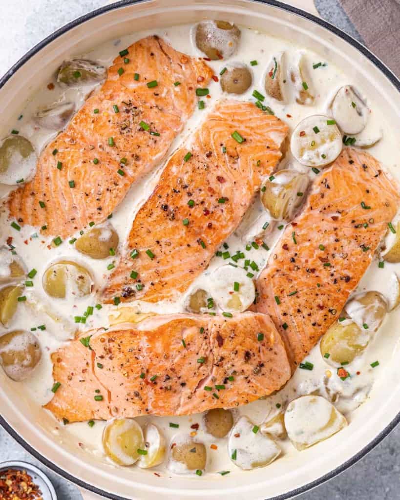 close up salmon in skillet with creamy potato sauce