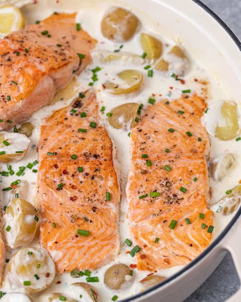 side shot of creamy salmon filet with potatoes in a pan