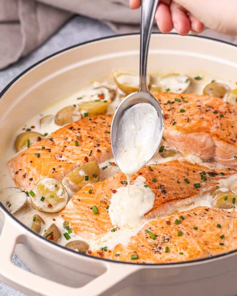 hand holding spoon to pour over creamy white sauce on salmon