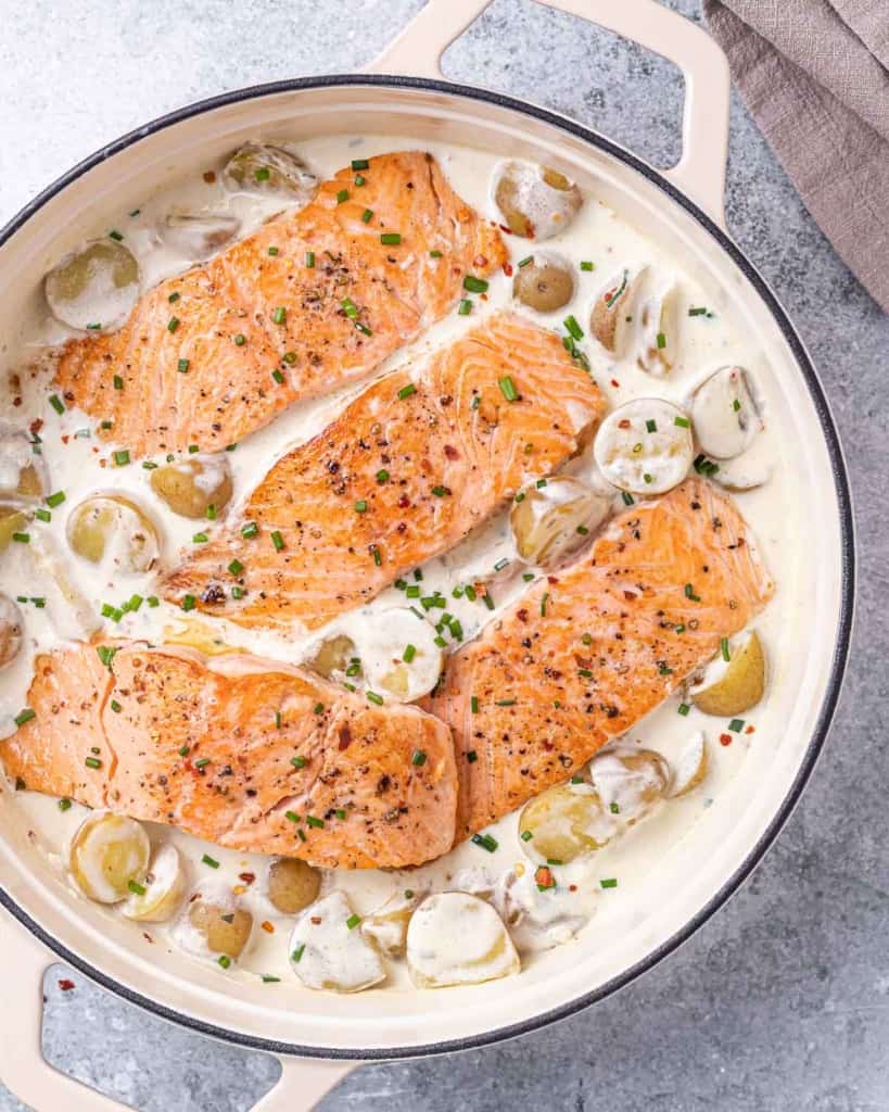 top view of salmon and potatoes in a creamy white sauce in a skillet