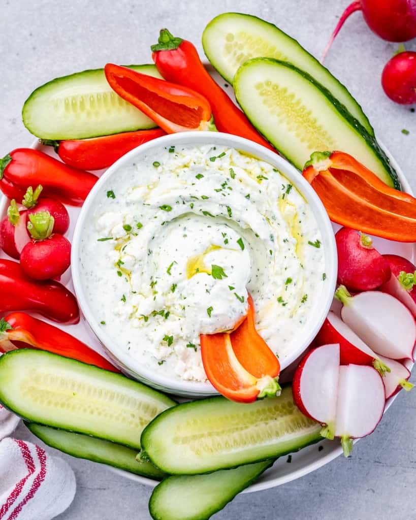 top view feta dip in a white bowl with sliced veggies on the side of the bowl