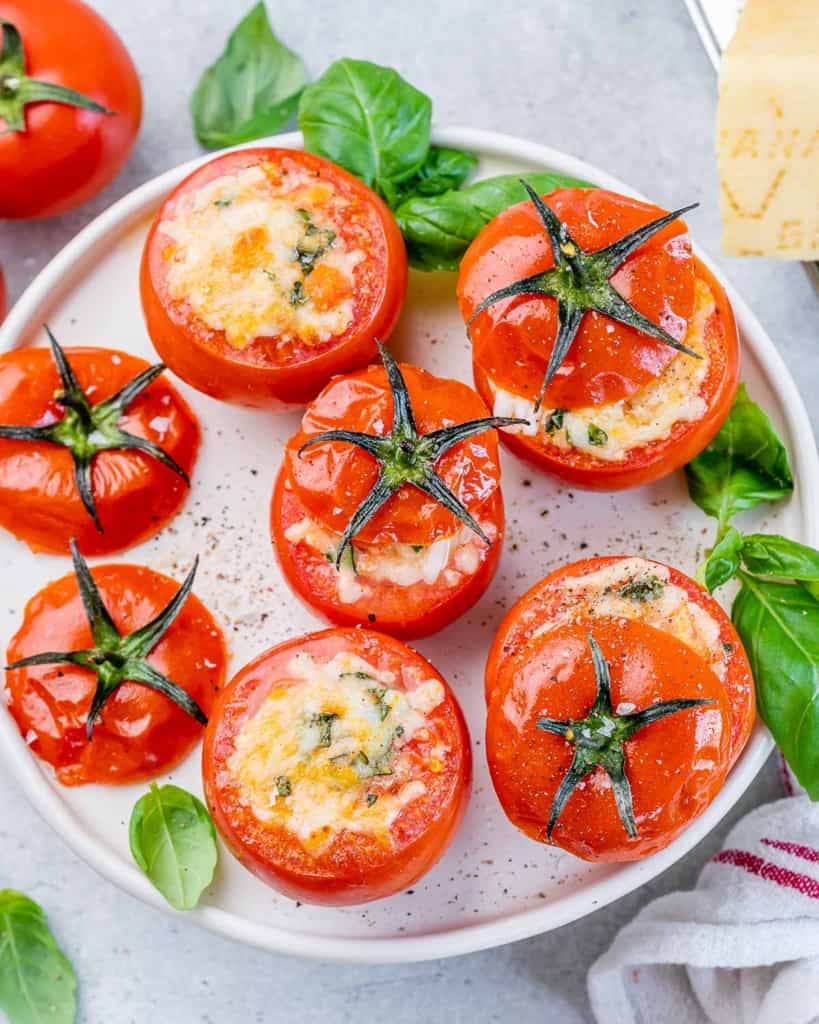 Top view baked tomatoes stuffed with cheese on a white plate.