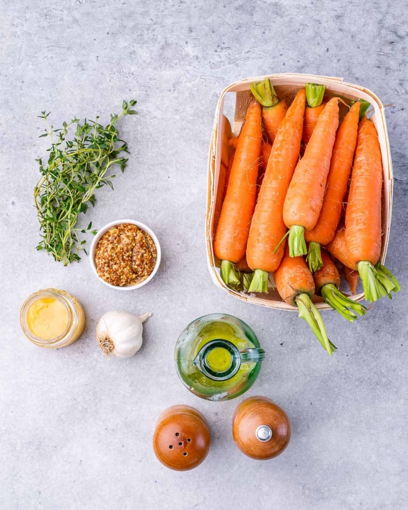 Uncooked carrots, olive oil, honey and mustard divided into bowls.