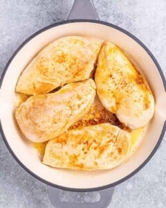 Seared chicken breasts in a skillet, lightly browned and seasoned.