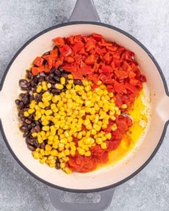 Overhead shot of diced tomatoes, corn, and black beans in a skillet with olive oil.