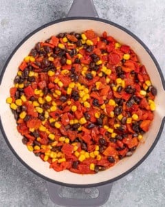 Skillet filled with black beans, corn, and roasted red peppers being cooked together.