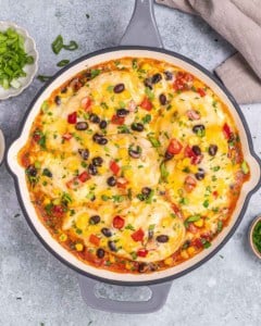 Top view of freshly baked Santa Fe chicken skillet with melted cheese, beans, corn, and colorful veggie toppings.