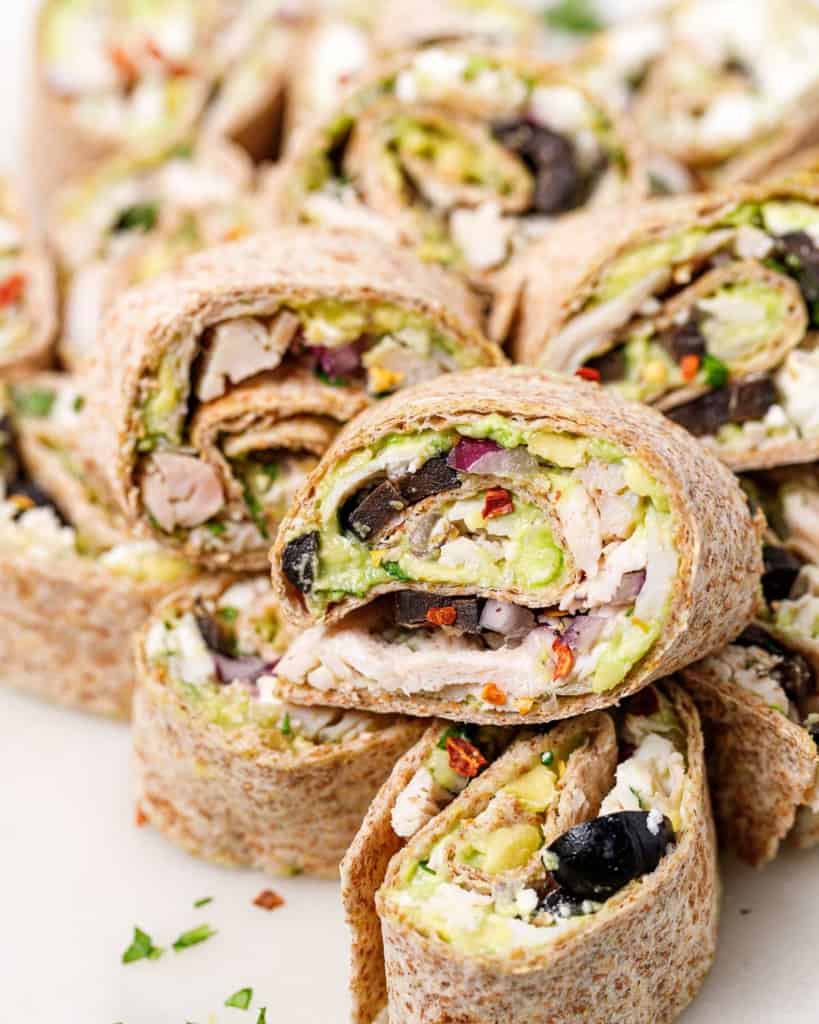 Avocado chicken salad pinwheels stacked on a plate.