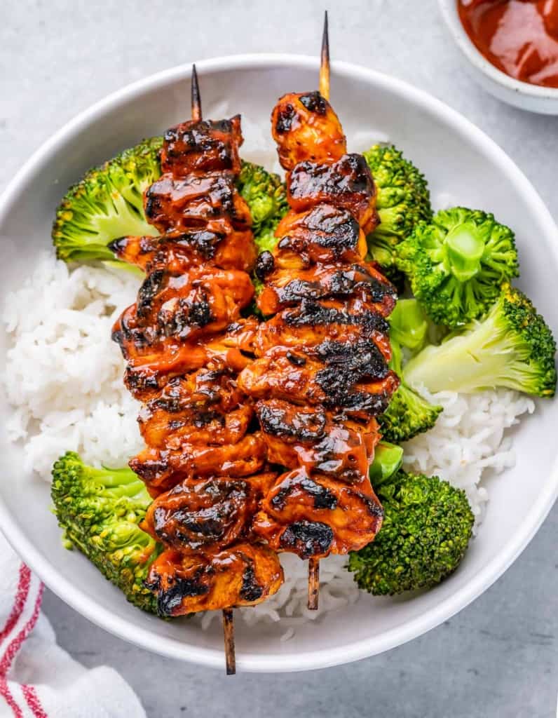 top view bbq chicken skewer served over a bowl of rice and sauteed broccoli in a round white bowl 