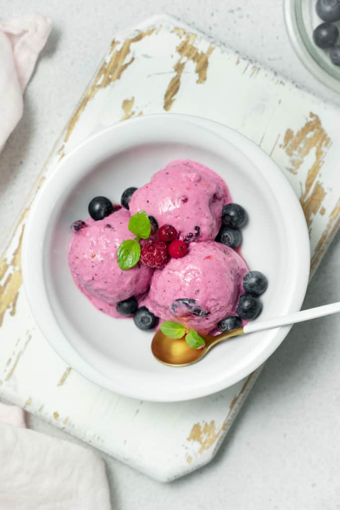 Three scoops of berry ice cream with fresh berries.