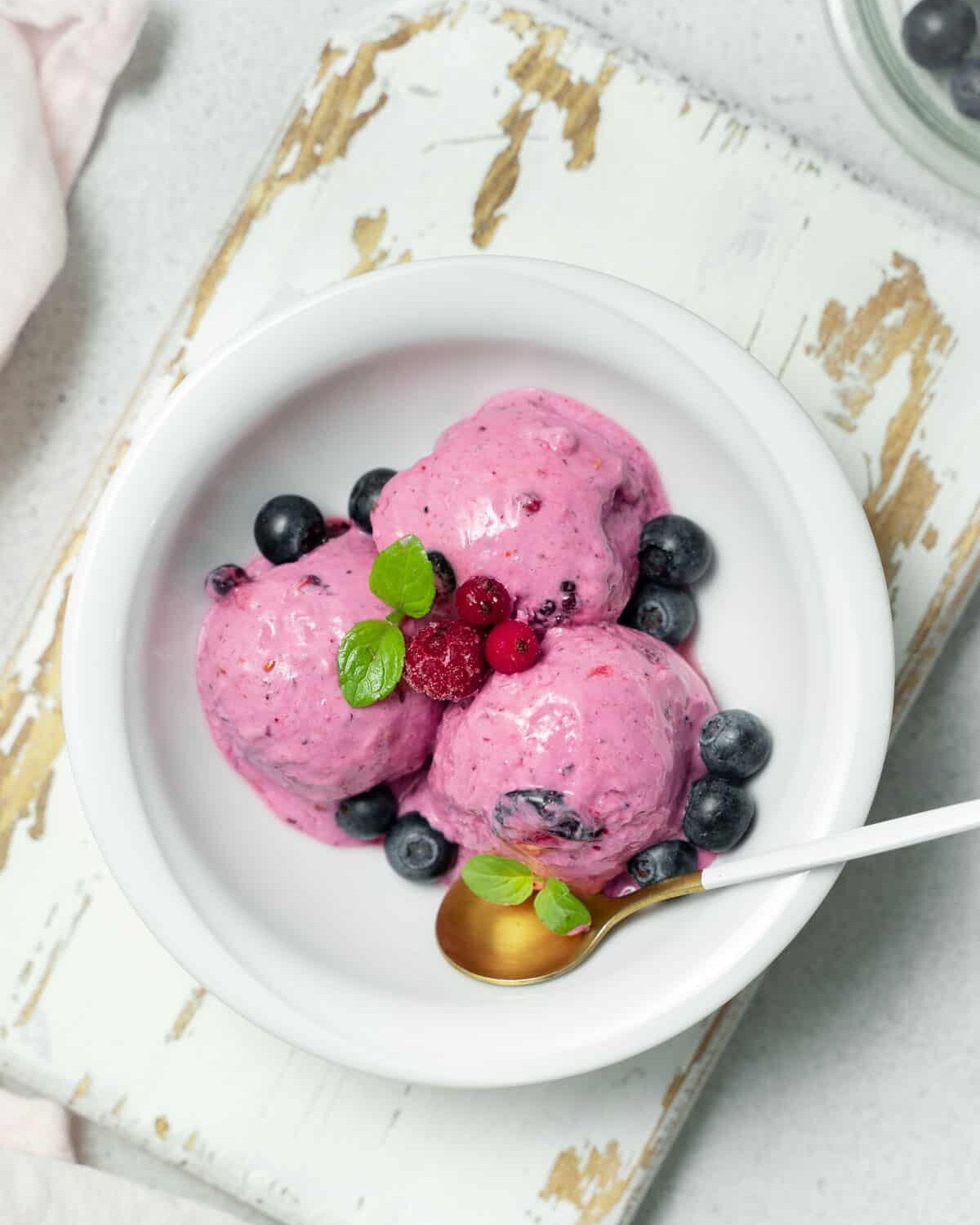 Three scoops of berry ice cream with fresh berries.