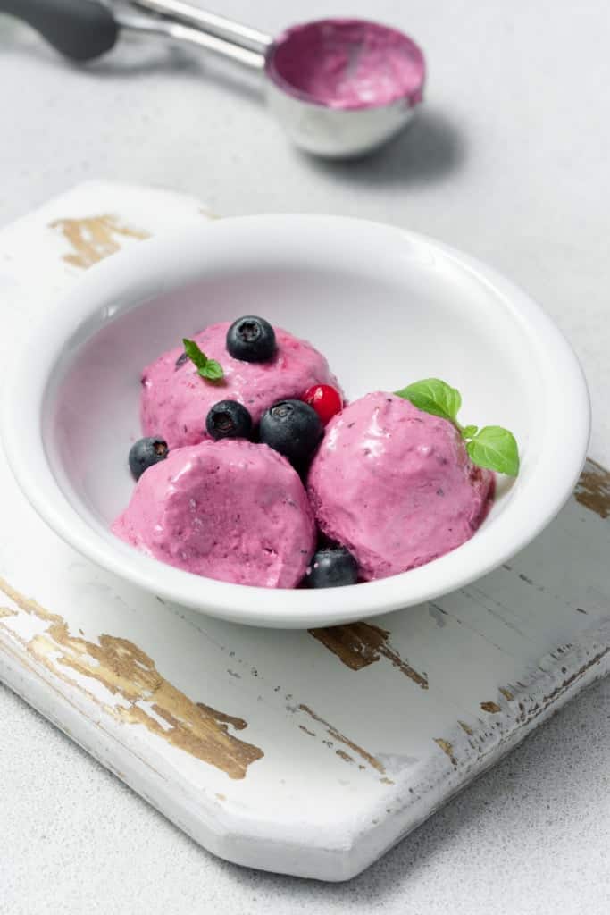 Three dollops of berries cottage cheese ice cream topped with fresh berries a white bowl.