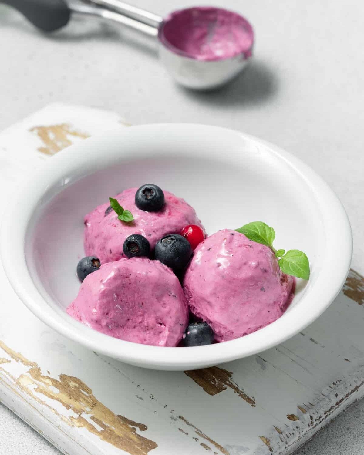 Three dollops of berries cottage cheese ice cream topped with fresh berries a white bowl.