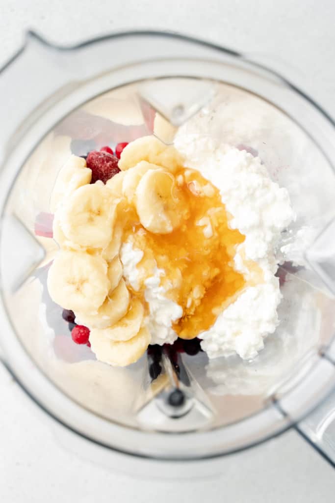 Frozen berries, cottage cheese, honey, and banana slices in a blender.