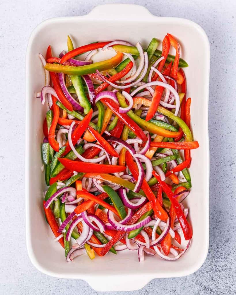 sliced peppers and onions in a white baking dish