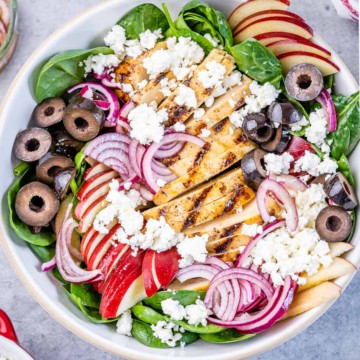 top view spinach salad in a bowl topped with grilled chicken feta cheese sliced apples and other veggies