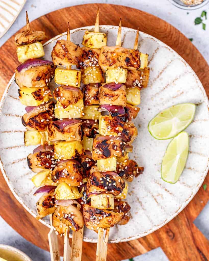 Grilled chicken skewers on a white plate with lime wedges.