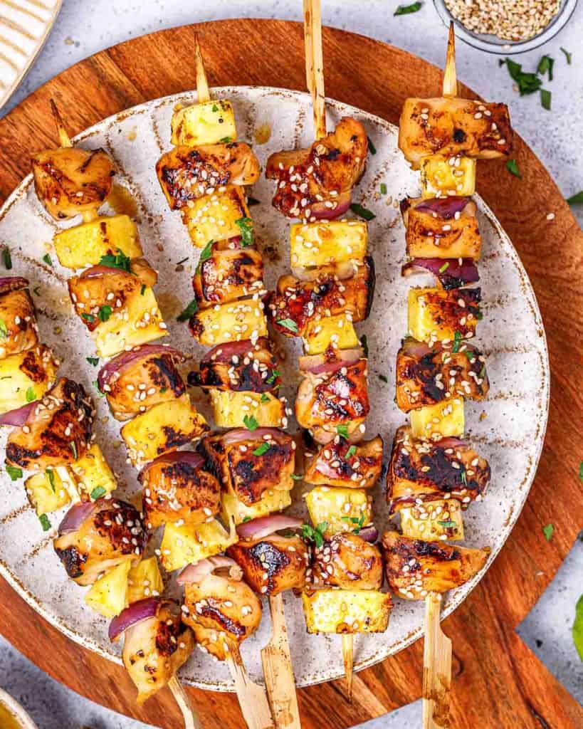 Top view of 5 grilled chicken skewers on a white round plate.