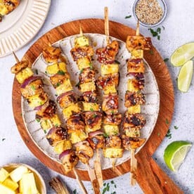 5 grilled chicken skewers on a white round plate.