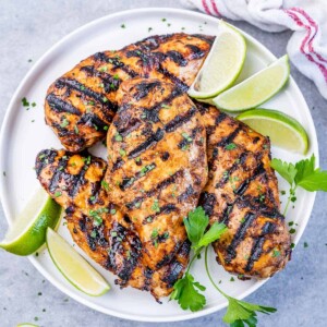 top view of grilled chicken breasts on a white plate with lime slices on the side for garnish