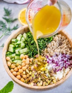 Pouring a lemon vinaigrette over a large salad.