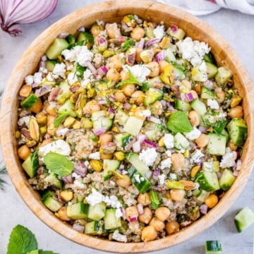 top view green salad with chickpeas topped with crumbled cheese in a wooden round bowl
