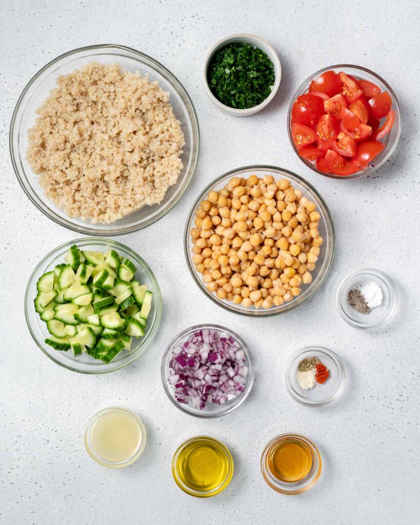 Quinoa, chickpeas, cucumber, tomatoes, onion, herbs, olive oil and seasonings divided into small bowls.