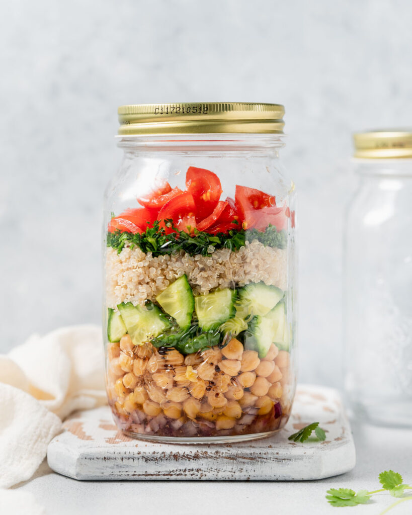 side shot of a salad jar with chickpeas, cucumber, quinoa, parsley and tomatoes with a lid over the jar