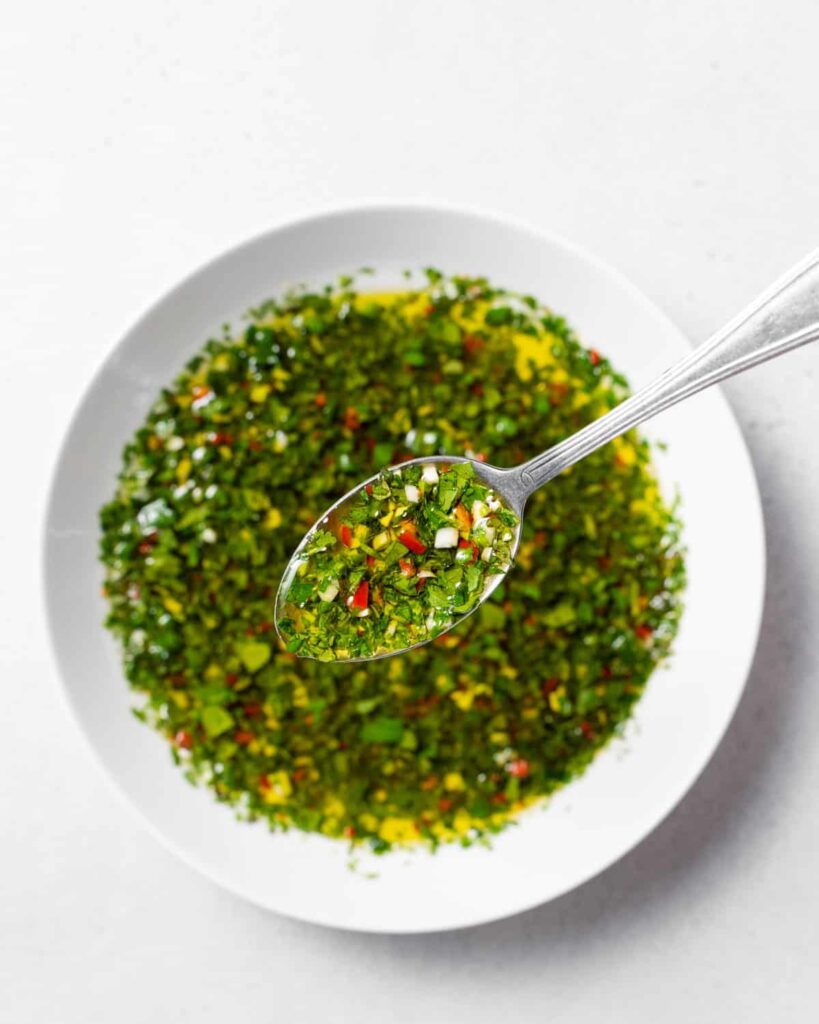 top view of a bowl of chimichurri sauce with a spoonful of sauce over the bowl