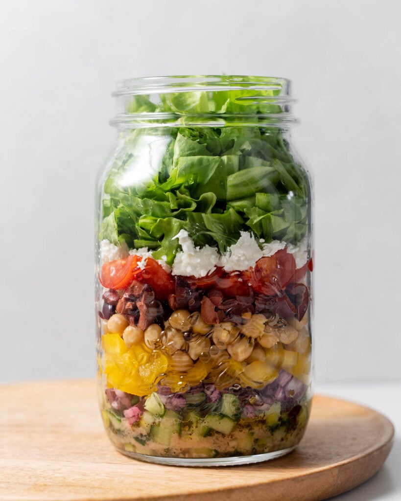 Ingredients to make greek salad added into a mason jar for meal prep