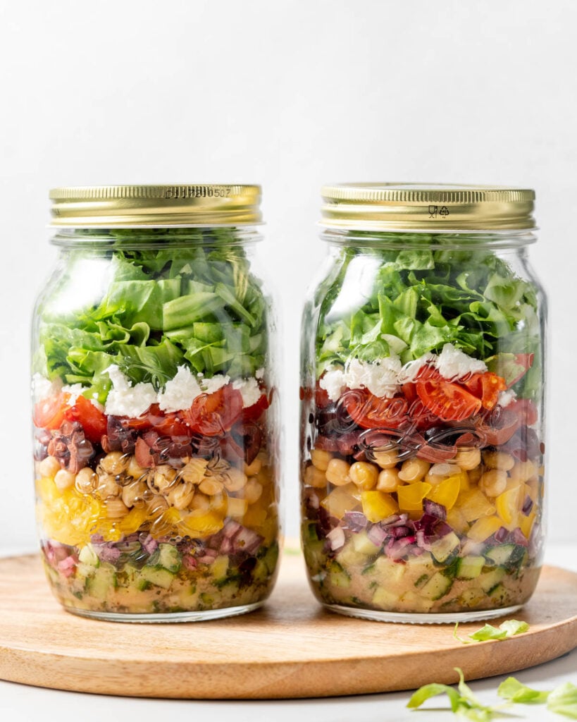 side shot of 2 jars filled with ingredients to make Greek salad 