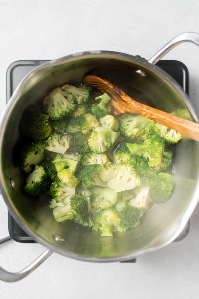Stirring cooked broccoli in a pot.
