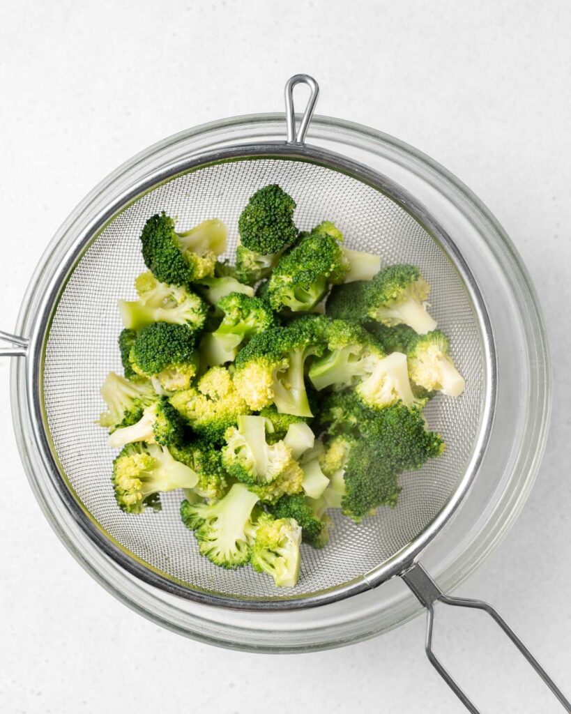 cooked broccoli in a sifter over an ice bath