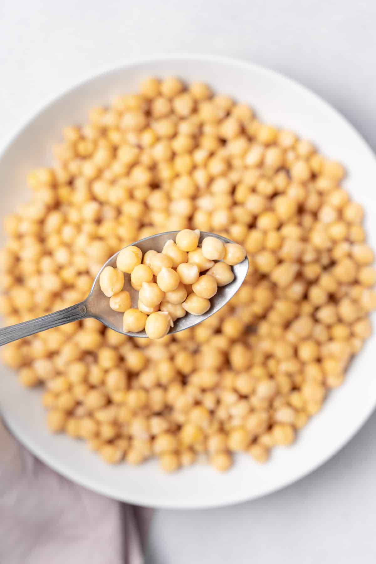 Spoonful of cooked chickpeas over a plate full of chickpeas.