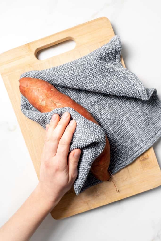 Patting a sweet potato dry with a kitchen towel.