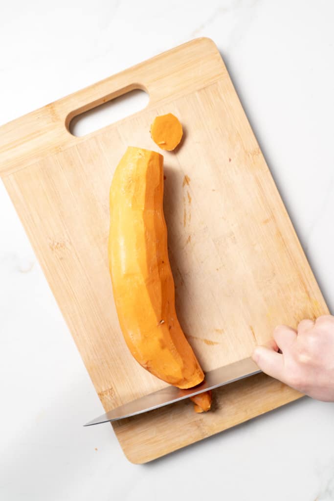 Using a knife to cut off the ends of a sweet potato.