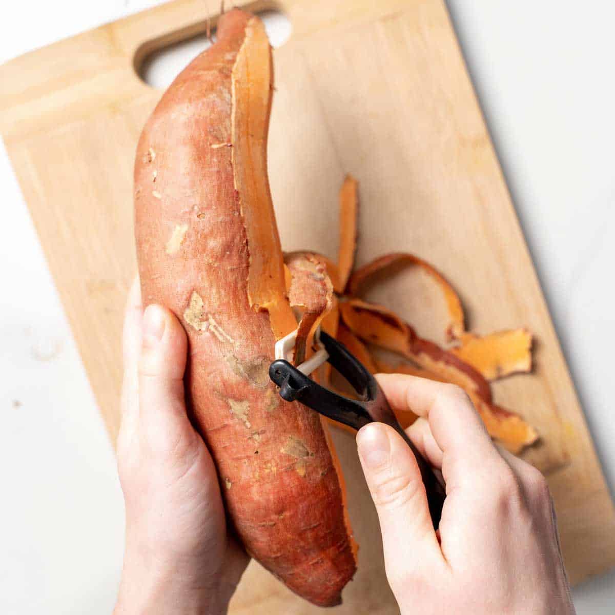 hand holding a sweet potato and another hand peeling the sweet potato with a peeler