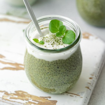 side shot of a jar with green match chia pudding topped with coconut yogurt with spoon in the jar